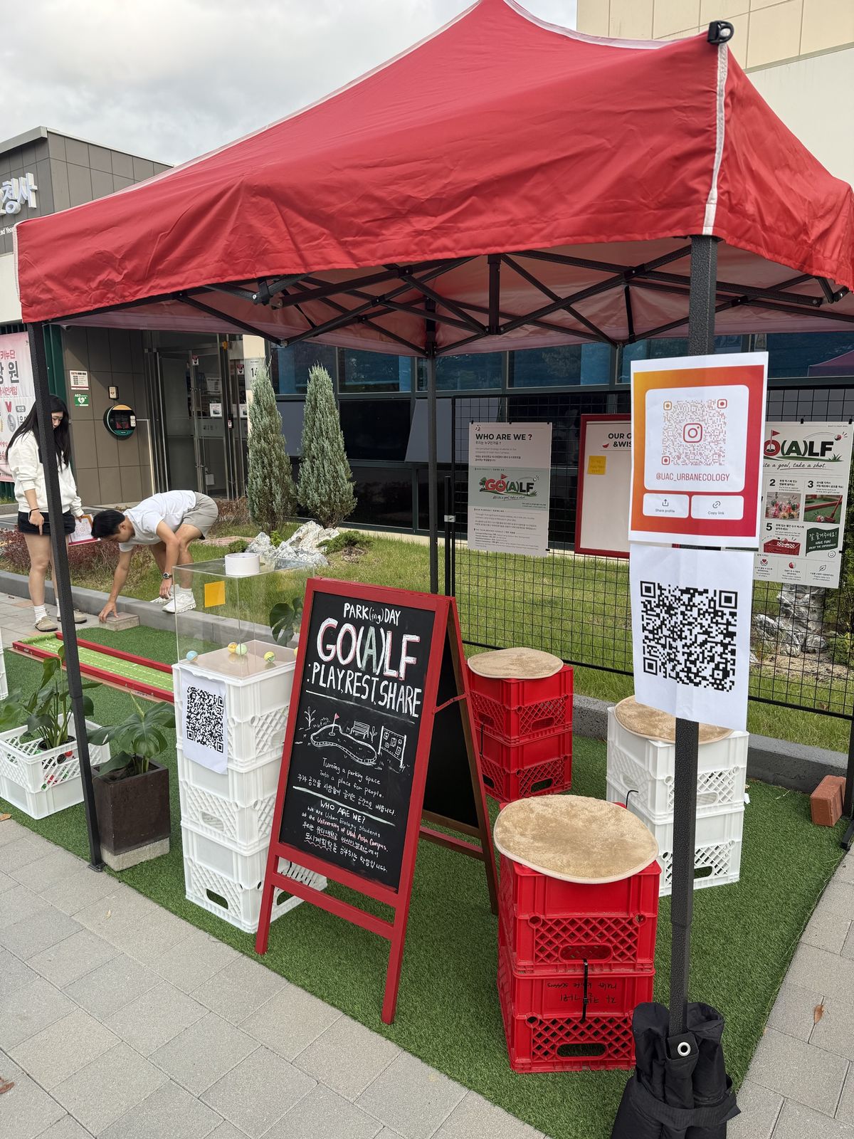 The booth under the red canopy: the chalkboard sign, the crate seating, the capsule box and the QR boards.